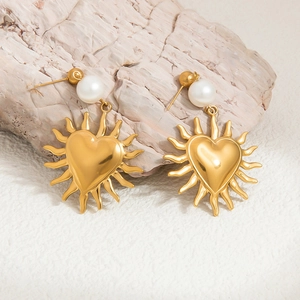 Macro view of gold heart sun earrings with pearls on a natural stone background