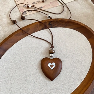 Close-up of vintage heart-shaped wooden pendant with white shell inlay and beaded cord