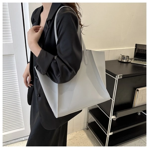 Close-up of a light grey PU leather tote bag worn by a model in a minimalist setting