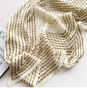 Detail of pleated silk scarf with gold and brown geometric stripes on white fabric