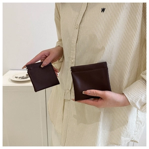 Detail of dark brown leather mini pouch with metal squeeze closure held by hand