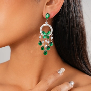 Close-up of butterfly stud earrings with green teardrop pendants on model's ear