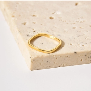Close-up of a minimalist golden square ring resting on a textured beige stone surface