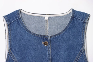Détail du col d'un gilet en jean avec étiquette taille S, bouton doré et surpiqûres oranges