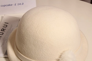 Close-up of beige wool beret featuring a fluffy pompom detail and soft felt texture