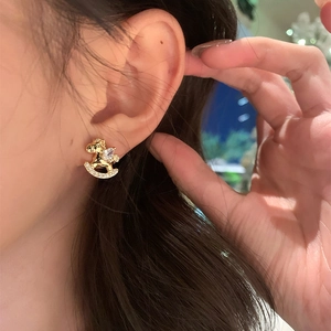 Detail of gold rocking horse stud earrings with cubic zirconia worn by a model