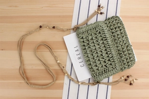 Detail of woven straw shoulder bag with green hollow pattern and decorative wooden beads