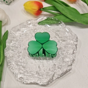 Detail of green acrylic clover hair claw clip on a glass plate with tulip flowers