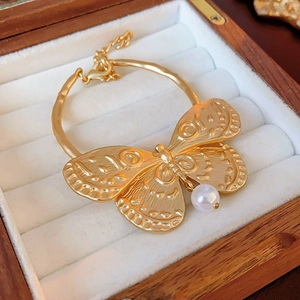 Detail view of a vintage gold butterfly cuff bracelet with a hanging white pearl