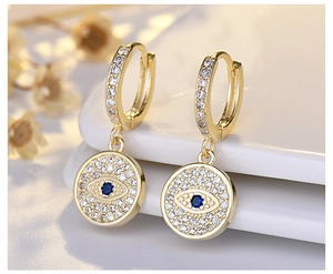 Close-up of golden evil eye earrings featuring blue gemstones and white zircon crystals