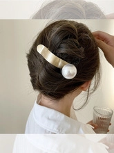 Detail of a gold metallic shark clip with a large white pearl in a hair styling scene