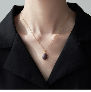 Close-up of a 18K gold plated titanium necklace with an oval purple gemstone pendant
