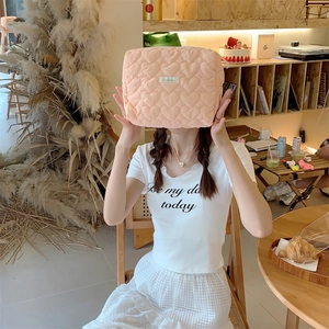 Detailed view of peach pink quilted heart cosmetics bag held by model in a cozy setting