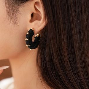 Close-up of black fabric wrapped C-shape earrings with gold bead accents on model