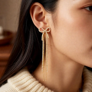 Detail of 18k gold plated bow tassel earrings with white zircon on a model
