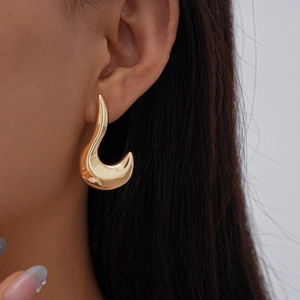 Detail of a gold irregular geometric earring with a polished finish worn by a model