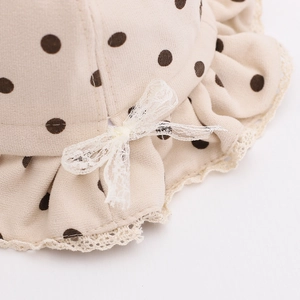 Détail d'un chapeau bébé beige à pois marron avec bordure en dentelle et nœud blanc