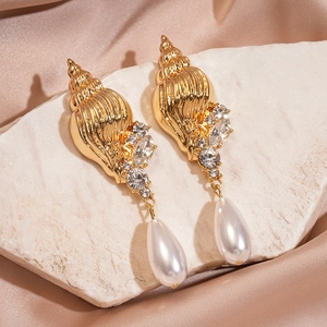 Golden conch earrings with sparkling rhinestones and teardrop pearls on silk fabric