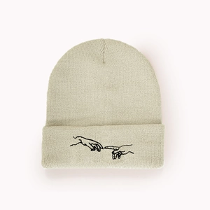 Détail du bonnet en maille crème avec broderie de mains noire inspirée de l'art classique