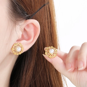 Elegant gold flower stud earrings with central pearl shown on a model's ear