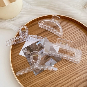 Detail of four transparent acrylic hair claws set in a stylish minimalist wooden tray