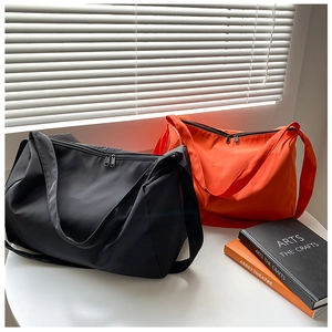 Detail of large nylon messenger bags in black and orange with wide straps and dual zippers