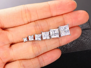 Detail view of six sizes of princess cut square zircon earrings held by hand