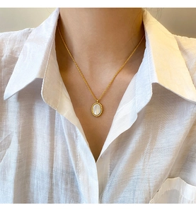 Close-up of elegant oval white mother-of-pearl pendant necklace with gold beaded edge