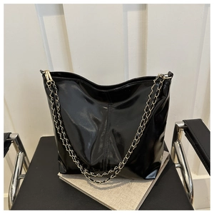 Detail of a black PU leather tote bag with gold chain strap on a black chair
