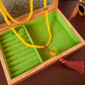 Vue détaillée du collier de perles jaunes avec pompon dans un écrin en bois et velours vert