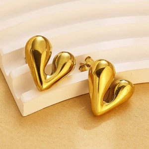 Vue détaillée de boucles d'oreilles dorées en forme de cœur abstrait sur socle beige