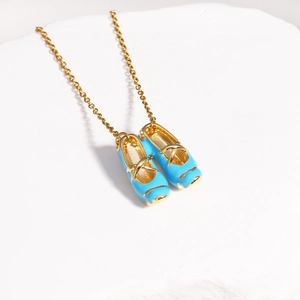 Detailed close-up of golden necklace with blue enamel ballet slippers on white stone