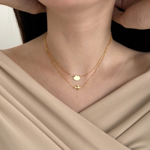 Detail view of a golden double-layer necklace with airplane and cloud charms on a model
