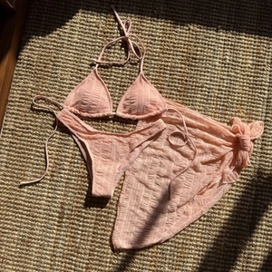 Flat lay of pink crinkle bikini set including top, bottom, and matching sarong detail