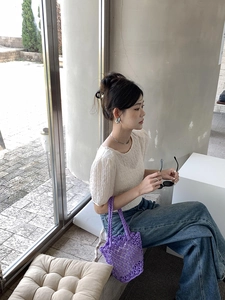 Detail of purple woven bucket bag styled with white puff-sleeve top and denim jeans