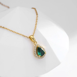 Macro shot of gold necklace featuring a pear-shaped green gemstone with small white diamonds