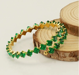 Detail of gold-plated wrap bracelet with square-cut emerald green zircons on wood stand