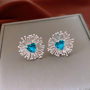 Macro detail of silver flower stud earring featuring a blue heart-shaped cubic zirconia