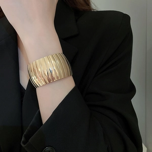 Detail of wide gold cuff bracelet featuring vertical textured stripes on model's wrist