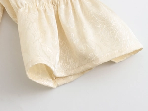 Détail des poignets élastiques à volants et texture jacquard florale sur robe beige