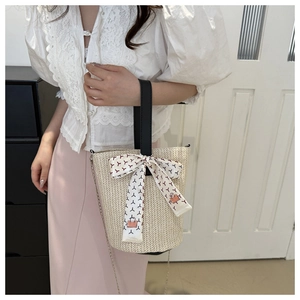 Détail du sac seau en paille avec ruban décoratif et poignée en cuir noir