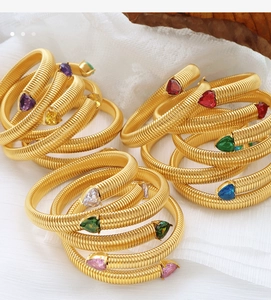 Detail of gold spiral snake bracelets featuring colorful heart-shaped gemstones on white gauze