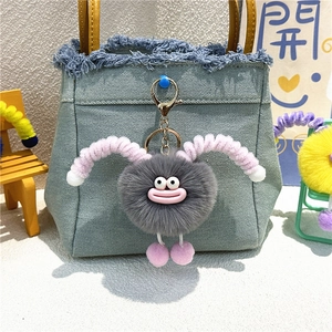 Cute grey plush monster keychain with pink horns hanging on a light blue denim bag