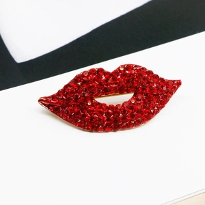 Macro shot of red rhinestone lips brooch with gold metal base on modern background