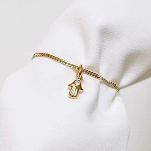 Gold Hamsa Hand bracelet with a clear zircon stone on a white fabric background
