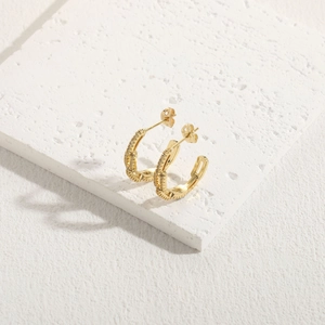 Detail of 14K gold plated C-shaped earrings with clear zircon stones on textured stone