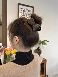 Brown knitted bow hair claw clip styled on a bun in a cozy home setting