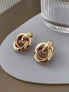 Close-up of golden geometric double-loop interlocking stud earrings on a textured base