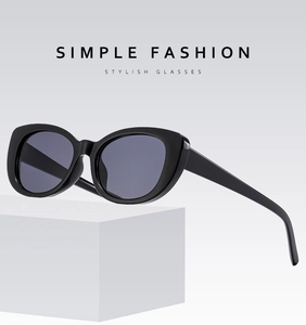 Close-up of black cat-eye sunglasses with gray lenses on a white geometric stand