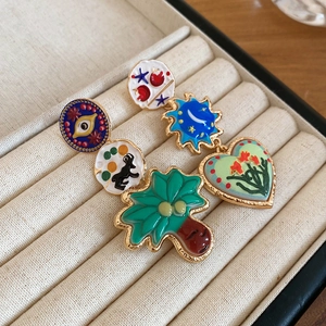 Detail of colorful enamel earrings with sun, moon and cat motifs on beige velvet display